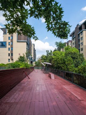 Modern bir apartman dairesinde, bahçenin yeşilliklerinin üzerinde yükselen, uzun, kırmızı tonlu ahşap bir geçitin dikey görüntüsü..