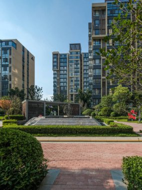 Dekoratif su çeşmesi, kırmızı tuğla yollar ve yüksek apartman binalarıyla modern bir konut bahçesinin dikey manzarası..