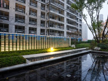 Geceleyin modern yapılandırılmış bir duvara karşı inşa edilmiş, mimari aydınlatmayı yansıtan sakin bir su yüzeyi. Görüntü gece sükuneti, mimari kesinlik ve meditasyonsal durgunluğu aktarıyor. Sığ alan derinliğine sahip yüksek kaliteli gerçek fotoğrafçılık.