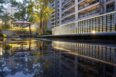 Akşamları parlayan bir duvar ve hala yansıtan bir havuzun yer aldığı modern bir manzara. Görüntü dinginliği, yapısal zarafeti, modern tasarımı ve huzurlu geceyi aktarıyor. Sığ alan derinliğine sahip yüksek kaliteli gerçek fotoğrafçılık.