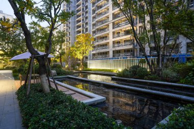 Akşamdan akşama geçiş sırasında ağaçların, bir su özelliğinin ve yumuşak ışıklı bir duvarın olduğu güzel bir avlu. Görüntü uyumu, doğal güzelliği, lüksü ve sükuneti temsil ediyor. Sığ alan derinliğine sahip yüksek kaliteli gerçek fotoğrafçılık.