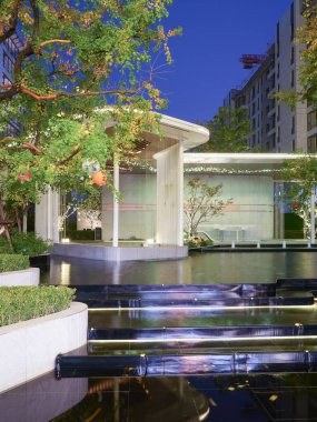 Modern bahçe köşkünün uzun, zarif manzarası ve gece gökyüzünün altındaki yansıtıcı havuzu. Görüntü yapısal karmaşıklığı, durgunluğu, derinliği ve lüks ambiyansı aktarıyor. Sığ alan derinliğine sahip yüksek kaliteli gerçek fotoğrafçılık.