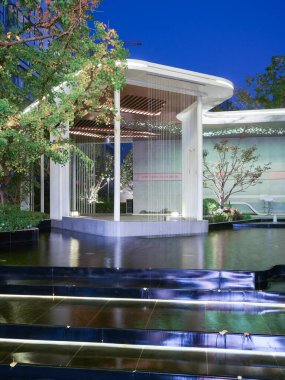 Bereketli yapraklarla çerçevelenmiş, durgun bir havuzda modern bir bahçe yapısının net bir gece yansıması. Görüntü meditasyonsal dinginliği, mimari güzelliği ve üst düzey dış tasarımı aktarıyor. Sığ alan derinliğine sahip yüksek kaliteli gerçek fotoğrafçılık.