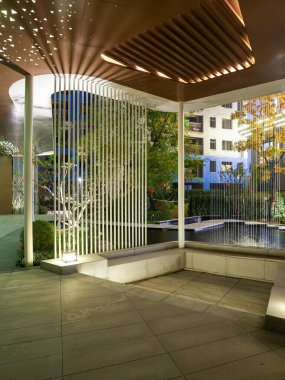 Huzurlu bir bahçede çarpıcı dikey yapısal çizgiler ve yumuşak zemin ışıklandırmasının yer aldığı modern bir açık hava pavyonu. Görüntüde düzen, sükunet, mimari hassasiyet ve meditasyon durgunluğu var. Sığ desenli yüksek kaliteli gerçek fotoğrafçılık