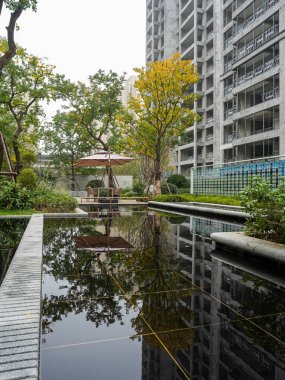 Yeşilliklerle çevrili modern bir mimari pavyonu mükemmel bir şekilde yansıtan sakin bir su yüzeyi. Görüntü barışı, lüksü, mimari dengeyi ve doğal güzelliği temsil eder. Sığ alan derinliğine sahip yüksek kaliteli gerçek fotoğrafçılık.