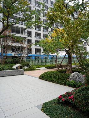 Geometrik taş kaldırımları, manikürlü çitler ve gür ağaçlarla dolu temiz, modern bir bahçe meydanı. Görüntü yapısal düzen, sükunet, üst düzey tasarım ve doğal konfor taşır. Sığ alan derinliğine sahip yüksek kaliteli gerçek fotoğrafçılık.