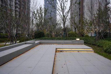 Günbatımında halka açık bir avluda modern taş basamaklar ve sıcak LED ışıklandırmalı oturma alanı. Görüntü, akşam sükunetini ve modern tasarımı aktarıyor. Doğal ışıklandırmalı yüksek kaliteli gerçek fotoğrafçılık.