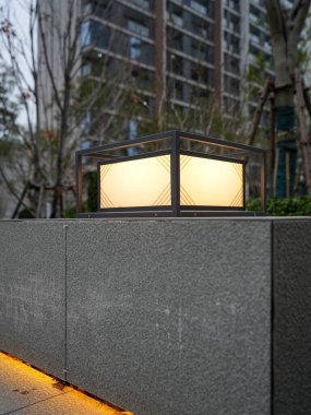 Parlayan modern bir açık hava lambasının detaylı görüntüsü ve dokulu taş bir duvarda gizli sıcak şerit aydınlatma. Görüntü zarif bir tasarım ve sıcak bir atmosfer sunuyor. Sığ alan derinliğine sahip yüksek kaliteli gerçek fotoğrafçılık.