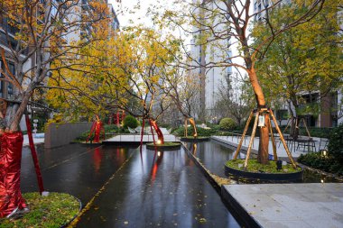 Günbatımında modern bir yerleşim bölgesinde sonbahar sarı yaprakları ve sıcak aydınlatmayı yansıtan sakin su özelliği. Görüntü doğal ahengi ve huzurlu bir akşamı temsil ediyor. Doğal ışıklandırmalı yüksek kaliteli gerçek fotoğrafçılık.