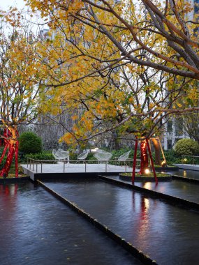 Sonbahar ağaçlarını yansıtan katmanlı yüzey havuzu ve alacakaranlıkta sakin bir konut avlusunda açık hava oturma alanı. Resim, boş bir yaşam tarzı ve zarif bir toplum ortamı sunuyor. Doğal ışıklandırmalı yüksek kaliteli gerçek fotoğrafçılık.