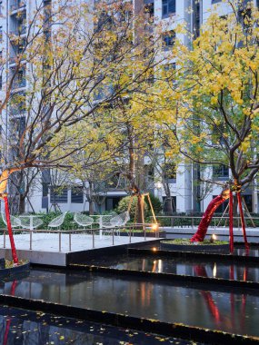 Sıcak sonbahar ağaçları ve beyaz teras sandalyeleri alacakaranlıkta katmanlı bir manzara havuzuna yansıyor. Görüntü zarif bir yaşam ve huzurlu bir akşam ortamı sunuyor. Doğal ışıklandırmalı yüksek kaliteli gerçek fotoğrafçılık.