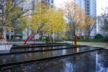 Şelale suları modern bir toplulukta yerleşim binalarını ve alacakaranlık gökyüzünün altındaki sonbahar yapraklarını yansıtır. Görüntü, huzurlu bir yaşam ve mimari güzelliği yansıtıyor. Doğal ışıklandırmalı yüksek kaliteli gerçek fotoğrafçılık.
