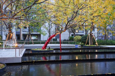 Lüks bir toplulukta alacakaranlıkta sonbahar ağaçlarını yansıtan katmanlı bir manzara havuzunun yanında modern açık hava oturma terası. Görüntü lüks yaşam tarzını ve huzurlu bir akşam atmosferini yansıtıyor. Doğal ışıklandırmalı yüksek kaliteli gerçek fotoğrafçılık.
