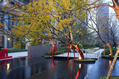 Parlak sonbahar ağaçlarıyla çevrili geniş bir yansıtma havuzu ve alacakaranlıkta lüks bir yerleşim bölgesinde oturma alanları. Görüntü, sakin bir ortam ve mevsimsel güzellikleri yansıtıyor. Doğal ışıklandırmalı yüksek kaliteli gerçek fotoğrafçılık