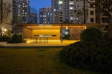Ilık LED ışıklandırma ile parlayan modern topluluk pavyonunun simetrik görüntüsü koyu mavi akşam gökyüzüne zıt. İmaj, şehir vahası ve modern mimari tasarımı taşır. Doğal ışıklandırmalı yüksek kaliteli gerçek fotoğrafçılık.