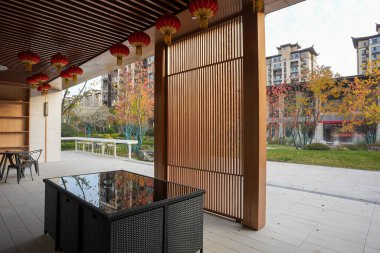 Ahşap bir köşkün gölgeli iç kısmından sonbahar ağaçlarıyla dolu huzurlu bir halk bahçesine bakıyor. Görüntü huzurlu bir geri çekilme ve ahenkli bir yaşam sunuyor. Doğal ışıklandırmalı yüksek kaliteli gerçek fotoğrafçılık.