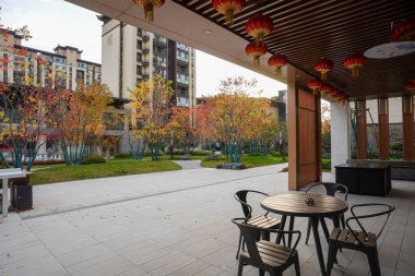 Yuvarlak masa ve sandalyeler modern bir pavyonun içinde ahşap bir tavan ve sakin bir avluya kırmızı fenerler asılıydı. Görüntü, topluluk toplanmasını ve kültürel birleşmeyi iletiyor. Doğal ışıklandırmalı yüksek kaliteli gerçek fotoğrafçılık.