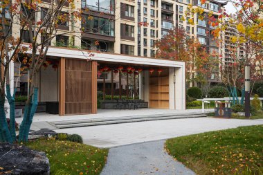 Puslu bir sonbahar bahçesinin yanında ahşap paneller ve kırmızı fenerlerin bulunduğu lüks bir konut manzarası. Görüntü lüks konutlar ve modern yaşam tarzını aktarıyor. Doğal ışıklandırmalı yüksek kaliteli gerçek fotoğrafçılık.