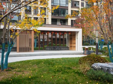 Huzurlu bir halk bahçesindeki yeşil çimlerin üzerinde ahşap ekranlar ve kırmızı fenerler bulunan modern açık hava pavyonu. Görüntü, kültürel rahatlık ve lüks yaşam tarzını aktarıyor. Doğal ışıklandırmalı yüksek kaliteli gerçek fotoğrafçılık.