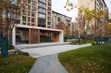 Etrafı sisli çimlerle ve yerleşim yerlerindeki sonbahar ağaçlarıyla çevrili şık ahşap bir pavyona doğru uzanan bir patika. Görüntü zarif bir toplum ve barışçıl bir ortam sunuyor. Doğal ışıklandırmalı yüksek kaliteli gerçek fotoğrafçılık.