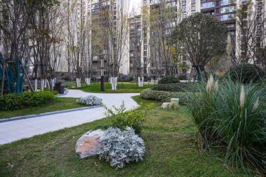 Temiz taş yolu manikürlü yeşil çimenler ve sakin bir yerleşim alanının bahçesinde dekoratif bitkiler arasında kıvrılıyor. Görüntü huzurlu bir mahalle ve modern bir manzara tasarımı sunuyor. Doğal ışıklandırmalı yüksek kaliteli gerçek fotoğrafçılık.