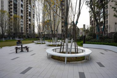 Geniş açı, birçok modern dairesel beyaz bankların ve ağaçların geniş asfalt bir plazada yerleşim alanı içinde sıralandığını gösteriyor. Görüntü, geniş bir toplum ve rahat bir açık hava konforu sağlıyor. Doğal lig ile yüksek kaliteli gerçek fotoğrafçılık