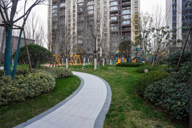 Aileye yönelik bir yerleşim bölgesinde renkli bir açık hava çocuk parkına giden eğimli bir kaldırım yolu. Görüntü, aile dostu çevre ve aktif yaşam tarzını aktarıyor. Doğal ışıklandırmalı yüksek kaliteli gerçek fotoğrafçılık.