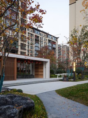 Büyük dekoratif kayaları ve sonbahar ağaçlarını geçerek şık bir ahşap halk köşküne uzanan sakin bir bahçe yolunun dikey görüntüsü. Görüntü zarif bir geri çekilme ve huzurlu bir mahalle olduğunu gösteriyor. Doğal ışıklandırmalı yüksek kaliteli gerçek fotoğrafçılık.