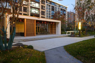 Alacakaranlıktaki sakin bir mahallede, sıcak ışıklı ahşap bir çim ve yeşil çimlerin yanında birleşen Paved ve çakıl yolları. Görüntü, ahenkli bir manzara ve lüks bir yaşam sunuyor. Doğal ışıklandırmalı yüksek kaliteli gerçek fotoğrafçılık.