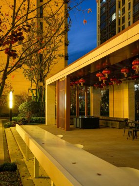 Parlak beyaz bar tezgahı, konut bahçesindeki mavi bir alacakaranlık gökyüzünün altında, modern ahşap bir pavyona doğru gidiyor. Görüntü lüks bir yaşam tarzı ve çağdaş bir eğlence sunuyor. Doğal ışıklandırmalı yüksek kaliteli gerçek fotoğrafçılık.