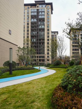 Modern bir yerleşim bölgesinde yeşil çimlerin arasından geçen kıvrımlı kaldırımlı bir yürüyüş yolunun yanında mavi boyalı bir koşu yolu. Görüntü aktif bir yaşam tarzı ve sağlıklı bir şehir ortamı sunuyor. Doğal ışıklandırmalı yüksek kaliteli gerçek fotoğrafçılık