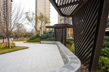 Çağdaş, koyu renkli gölgeli bir yapının altından, kaldırımlı bir yol ve yeşil bir çimenlik boyunca detaylı bir görüş. Görüntü mimari ayrıntıları ve zarif dış tasarımı aktarıyor. Doğal ışıklandırmalı yüksek kaliteli gerçek fotoğrafçılık