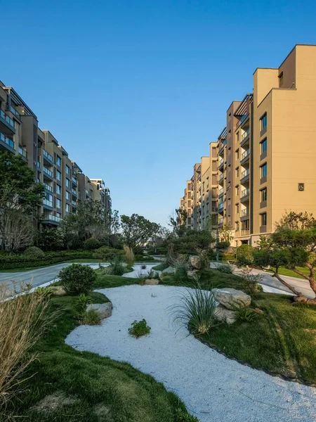 Beyaz çakıllar, doğal taşlar ve modern apartman binalarına karşı döşenmiş manikürlü çalılarla dolu huzurlu bir Zen bahçesi manzarası..