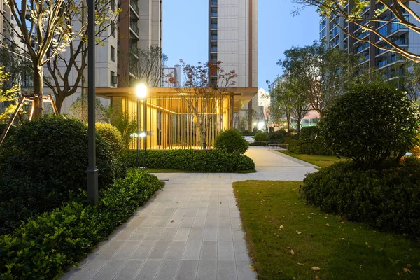 Mavi saat boyunca sakin bir halk bahçesinde parıldayan modern bir açık hava köşküne doğru uzanan taştan yürüyüş yolu. Görüntü, mahalleyi ve güvenli çevreyi karşılıyor. Doğal ışıklandırmalı yüksek kaliteli gerçek fotoğrafçılık.