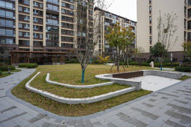 Çağdaş bir yerleşim bölgesinde eğimli taş manzara duvarları ve manikürlü yeşil çimenler geniş görünüm. Görüntü, yapılandırılmış çevreyi ve uyumlu yaşamı aktarır. Doğal ışıklandırmalı yüksek kaliteli gerçek fotoğrafçılık.