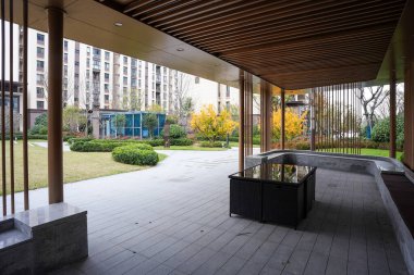 Dağılmış ahşap bir pavyonun altından huzurlu yeşil bir avluya ve modern bir toplulukta asfaltlanmış bir plazaya bakıyor. Görüntü açık havada rahatlık ve özel konfor sağlıyor. Doğal ışıklandırmalı yüksek kaliteli gerçek fotoğrafçılık.