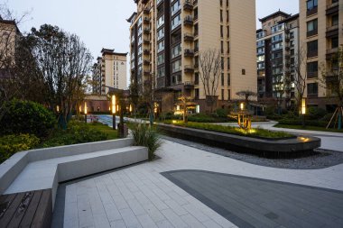 Alacakaranlıkta huzurlu bir halk bahçesinde kıvrımlı oturma yerleri ve sıcak zemin ışıklarıyla çevrili sarmal taş kaldırım. Görüntü huzurlu bir ortam ve modern peyzaj mimarisi sunuyor. Doğal ışıklandırmalı yüksek kaliteli gerçek fotoğrafçılık.