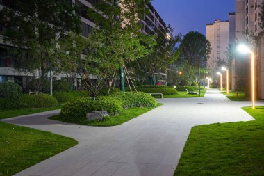 Modern demirbaşlarla aydınlatılan ve yemyeşil gece yeşillikleriyle çevrili, meskun bir bahçede ışıldayan bir yol. Görüntü huzur, akşam keyfi, toplum ve huzurlu şehir yaşamını aktarıyor. Sığ alan derinliğine sahip yüksek kaliteli gerçek fotoğrafçılık.