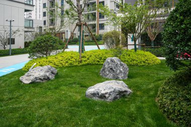 Bir yerleşim bölgesinde pürüzsüz dekoratif taşlar, gür yeşillik ve parlak yeşillikler içeren peyzajlı bir bahçe yatağı üzerinde yoğunlaşmak. Görüntü organik güzelliği, bahçe bakımını, sakin manzara tasarımını ve doğal dengeyi yansıtıyor. Yüksek kaliteli gerçek fotoğrafçılık.