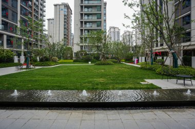 Etrafı yeşil çimlerle çevrili sakin, yansıtan bir su havzası ve modern konut mimarisi. Resim, huzurlu bir toplum hayatı, doğa bütünleşmesi, mekansal tasarım ve sükunet içeriyor. Sığ alan derinliğine sahip yüksek kaliteli gerçek fotoğrafçılık