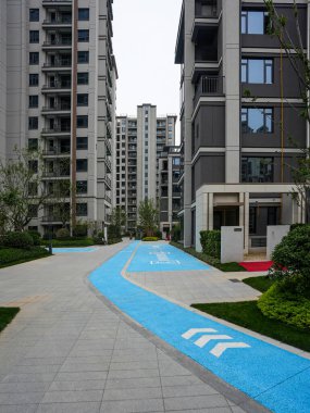 Modern apartman binaları arasında uzanan mavi bir patikanın geniş açılı görüntüsü. Görüntü şehir hareketini, toplum tasarımını, aktif yaşamı ve mimari ölçekleri aktarır. Kaliteli gerçek fotoğrafçılık ve sığ görüntü.