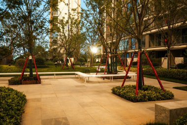 Sıcak altın saat ışığında parlayan, taştan koltukları ve güneş lekeli ağaçlarıyla huzurlu bir bahçe alanı. Görüntü sıcaklığı, doğal güzelliği, dinginliği ve dışarıdaki konforu yansıtıyor. Sığ alan derinliğine sahip yüksek kaliteli gerçek fotoğrafçılık.