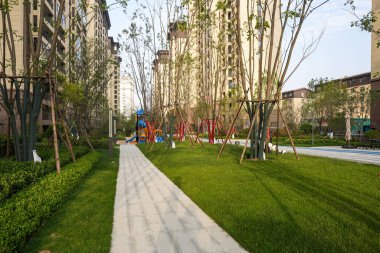 Manikürlü çalılar ve ağaçlarla çevrili, modern bir mesken parkında kıvrılan güzel, güneşli bir taş geçit. Görüntü huzurlu şehir yaşamını, tasarım düzenini, doğa entegrasyonunu ve temiz havayı aktarıyor. Sığ ve yüksek kaliteli gerçek fotoğrafçılık