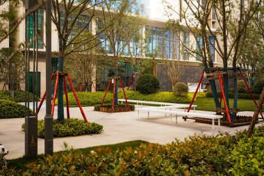 Modern beyaz taş bankları ve yemyeşil yemyeşil bahçeleri olan, sıcak gün ışığında yakalanmış, parlak, temiz bir bahçe alanı. Görüntü basitliği, sakinliği, mimari tasarımı ve barışçıl açık hava yaşamını aktarır. Sığ d ile yüksek kaliteli gerçek fotoğrafçılık