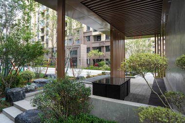 Üzerinde taş basamaklar ve olgun çalıların bulunduğu, ahşap aksanlı, rafine bir bahçe köşkü. Görüntü sakin, yapısal tasarım, açık havada yaşam ve konut huzurunu iletir. Sığ derinlikli yüksek kaliteli gerçek fotoğrafçılık