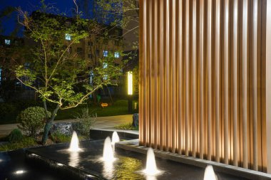 Sessiz bir akşam bahçesinde parlayan bir su özelliğinin yanında modern mimari dikey sütunların yakın çekimi. Görüntü ritmi, tasarım karmaşıklığını, huzuru ve üst düzey konut estetiğini aktarıyor. Yüksek kaliteli gerçek fotoğrafçılık ile Will