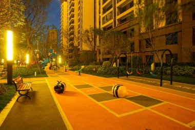 Canlı bir çocuk açık hava aktivitesi parkı. Parlak, renkli oyun ekipmanları var. Huzurlu bir akşam bahçesi ortamında geçiyor. Görüntü neşe, toplum güvenliği, aktif aile yaşam tarzı ve modern yerleşim tasarımı taşır. Yüksek kalite gerçek ph