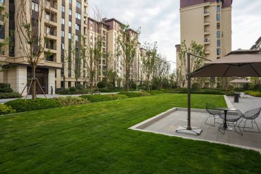 Modern apartmanlara karşı yeşil çimenli ve açık verandalı sakin, güneşli bir park alanı. İmaj rahatlamayı, toplumsal refahı ve huzurlu günlük yaşamı iletir. Sığ derinliğe sahip yüksek kaliteli gerçek fotoğrafçılık