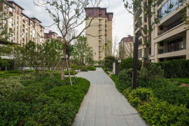 Manikürlü çitlerle ve ağaçlarla çevrili yemyeşil bir bahçe parkının içinden geçen açık bir taş yol. Görüntü doğal sükuneti, tasarım düzenini, barışçıl yürüyüşü ve şehir yeşilliğini aktarıyor. Sığ ve yüksek kaliteli gerçek fotoğrafçılık