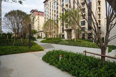 Modern bir yerleşim parkındaki yükseltilmiş yeşil alana uzanan taş basamakların huzurlu manzarası. Görüntü yapısal dengeyi, tazeliği, mimari tasarımı ve dingin doğayı taşır. Sığ alan derinliğine sahip yüksek kaliteli gerçek fotoğrafçılık.